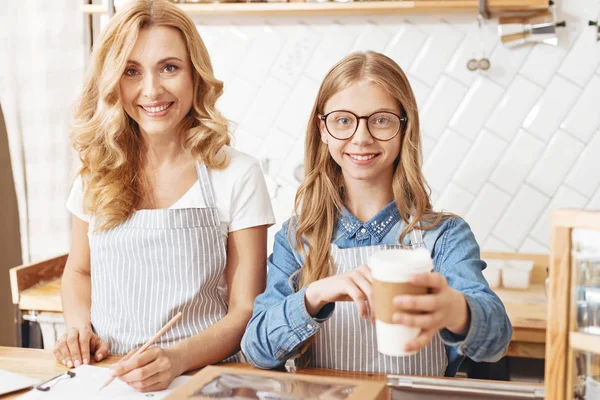 Radiante madre e hija sonriendo al cliente en la cafetería —  Fotos de Stock