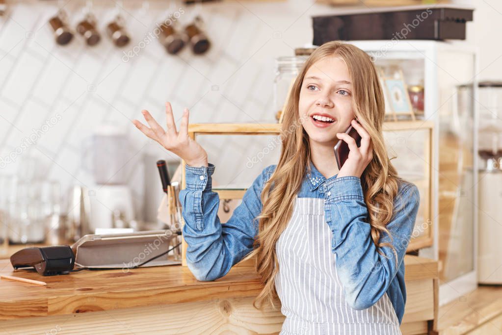 Emotional young lady in apron gesturing during phone talk