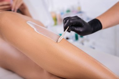 Depilatory krem istemci bacaklarına koyarak siyah eldivenli kadın
