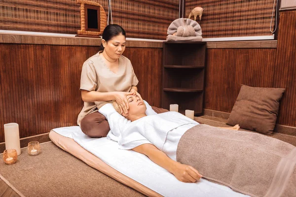 Ernste asiatische Frau sitzen in der Nähe ihrer Kunden Kopf — Stockfoto