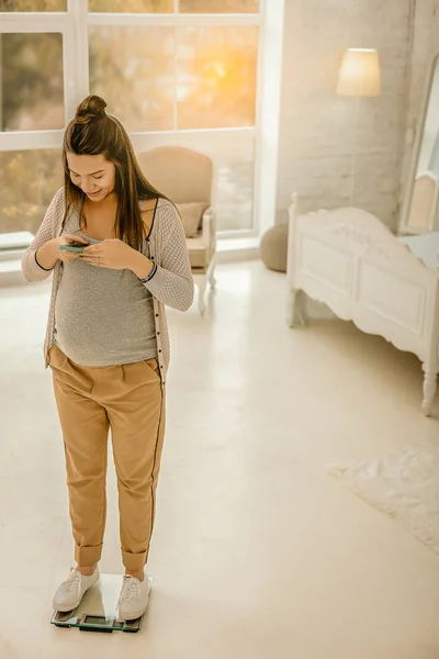 Gravid kvinna stående på vikterna och inspelning hennes vikt — Stockfoto