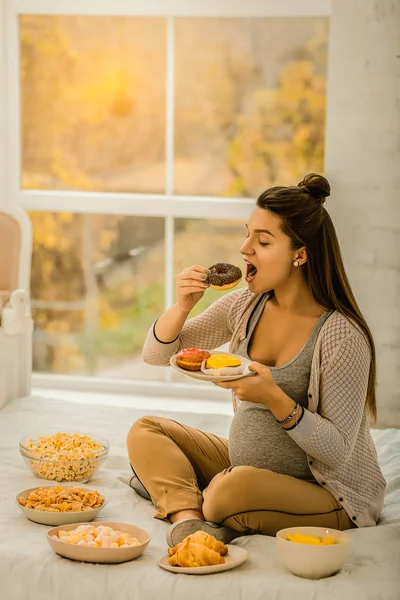 Schwangere isst Krapfen und andere Süßigkeiten — Stockfoto