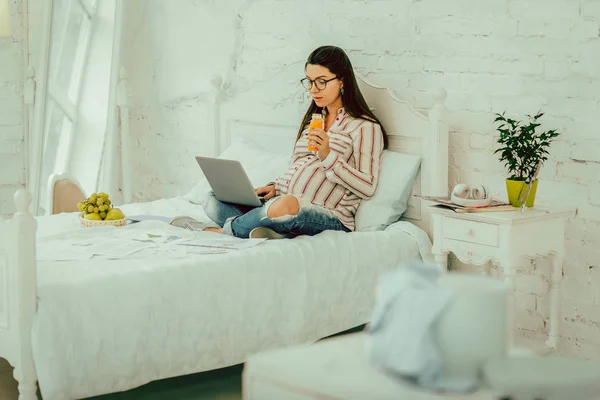 Mujer embarazada bebiendo un jugo y trabajando remotamente —  Fotos de Stock