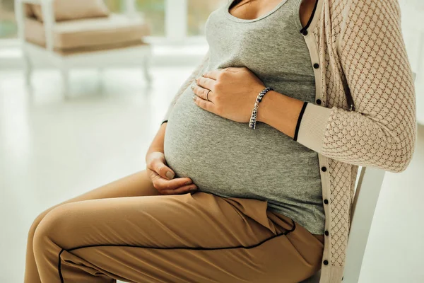 Kvinna sitter och vidrör hennes gravida mage — Stockfoto