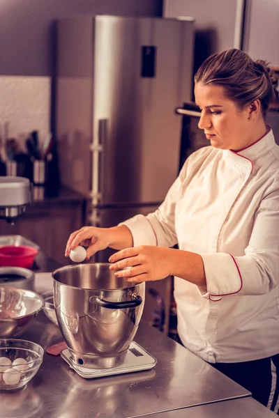 Mooie geschoolde vrouwelijke chef-kok het ei te breken — Stockfoto