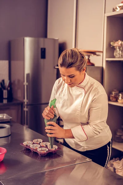 Geschoolde mooie vrouw met behulp van een spuitzak voor muffins — Stockfoto