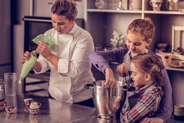 Positivo encantado hijas ayudando a su mamá en la cocina —  Fotos de Stock