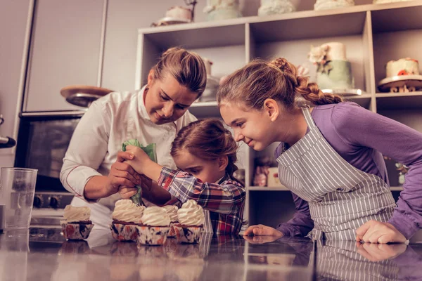 Deleitado agradable niñas poniendo crema en cupcakes —  Fotos de Stock