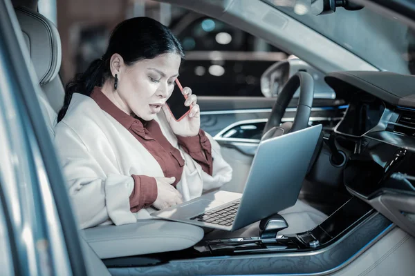 Успешная взрослая деловая женщина, сидящая в машине и пользующаяся ноутбуком — стоковое фото
