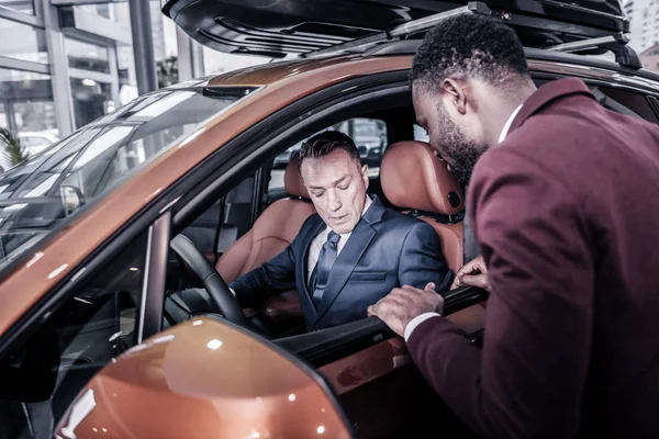 Бородатый менеджер по продажам автосалона, стоящий рядом с клиентом, сидящим в машине — стоковое фото