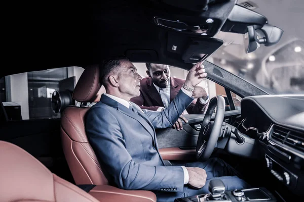 Стильный взрослый мужчина с ручными часами, смотрящий в зеркало автомобиля — стоковое фото