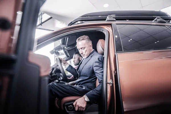Empresario empujando su asiento hacia atrás mientras está sentado en un coche nuevo — Foto de Stock