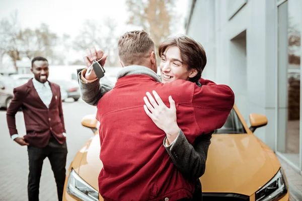 Χαρούμενος νεαρός γιος που αγκαλιάζει τον πατέρα του μετά την παραλαβή του τα κλειδιά του αυτοκινήτου — Φωτογραφία Αρχείου