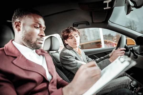 Bearded driving instructor putting marks after test driving