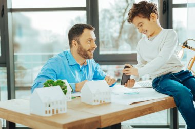 Buraya bak. Masada oturan ve modern bir cihazla oturan oğlu gülümseyen dikkatle bakarak sakin çalışan mühendis