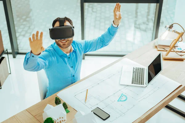 Virtual reality. Emotional progressive engineer putting his hands up and smiling while using virtual reality glasses in his work