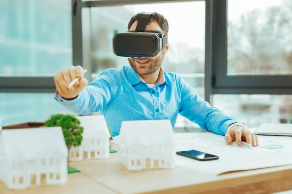 Engenheiro positivo apontando para uma casa em miniatura e sorrindo — Fotografia de Stock