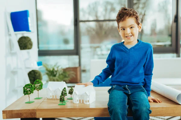 Fröhlicher Junge sitzt auf dem Tisch und spielt mit Miniaturhäusern — Stockfoto