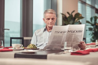 Hoş yaşlı adam öğle yemeği yerken bir gazete okuyor