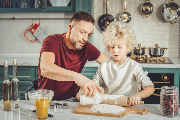 Dark-haired father adding some flour to dough for future pie