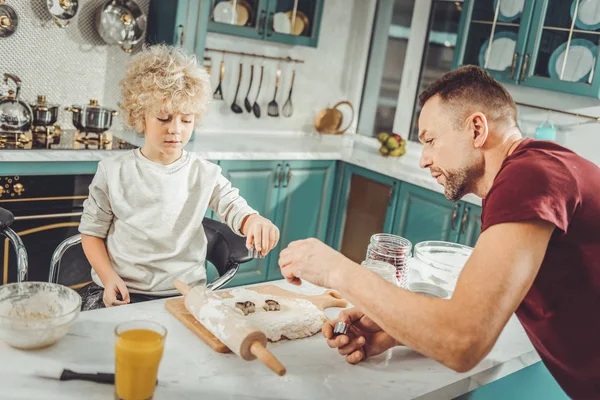 Pequeño hijo usando latas para hornear mientras forma galletas con su padre — Foto de Stock