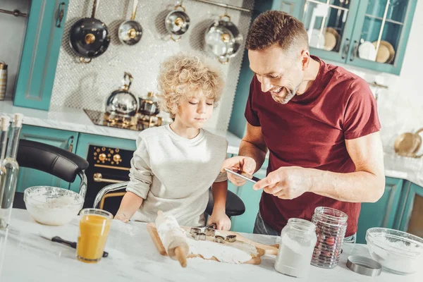 笑みを浮かべて男の息子と一緒に料理をしながら将来のクッキーの写真を作る — ストック写真
