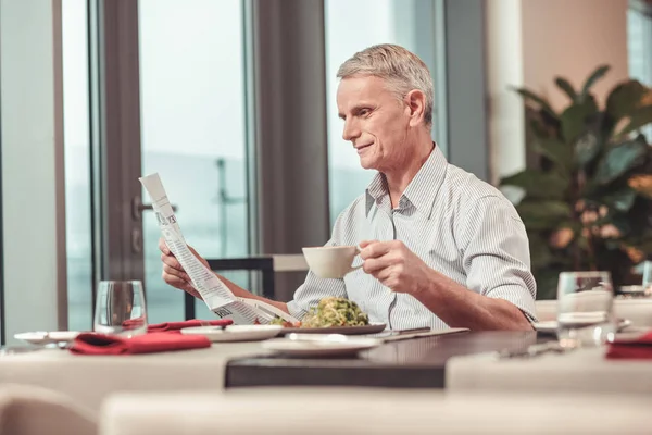 Концентрований чоловік читає статтю під час пиття кави в ресторані — стокове фото