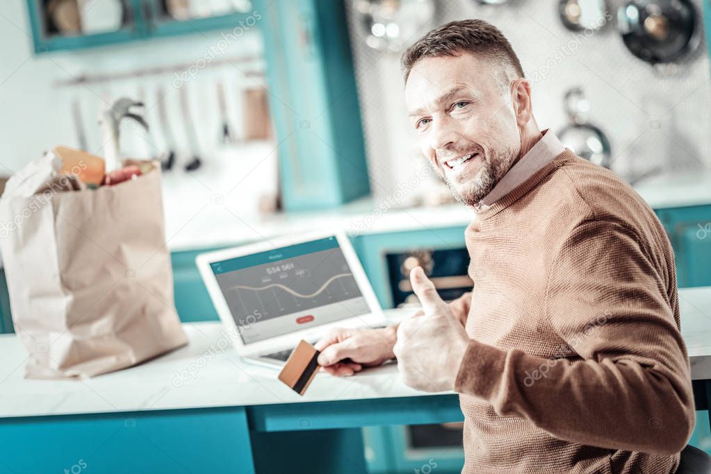 Pleased bearded man raising thumb up at home