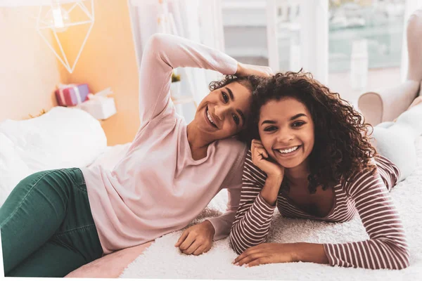 Meninas sorridentes de cabelos escuros deitado na cama no quarto espaçoso luz — Fotografia de Stock