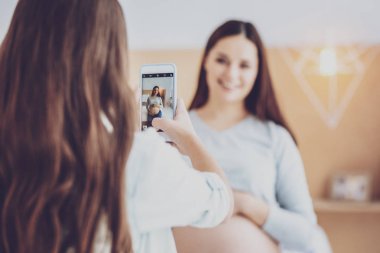 Dalgalı saçlı kız alarak fotoğraf bir telefon ile hamile anne