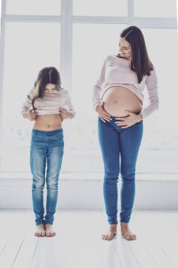 Neşeli hamile kadın ve kızı ile çıplak bir karınla poz