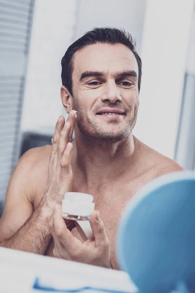 Радостный брюнетка мужчина наносит крем на лицо — стоковое фото