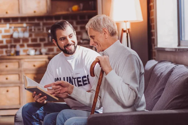 Очарованный волонтер, читающий книгу для пенсионера — стоковое фото