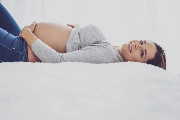 Счастливая беременная женщина лежит на кровати и улыбается — стоковое фото