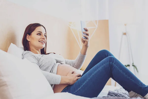 Glad gravid kvinna tar selfie på säng — Stockfoto