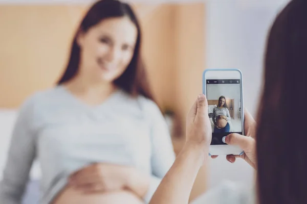 Chica preadolescente tomando fotos de una mujer embarazada sentada en la cama — Foto de Stock