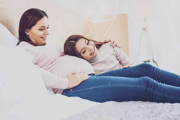 Söt preteen flicka och hennes gravida mamma myser på sängen — Stockfoto