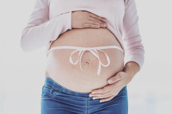 Nahaufnahme einer schwangeren Frau, die mit Schleife am Bauch posiert — Stockfoto