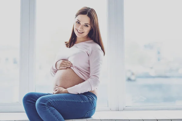 Красивая беременная женщина сидит на подоконнике — стоковое фото