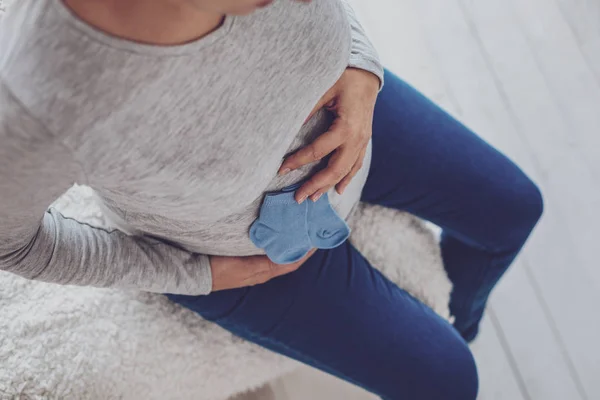 Pandangan utama wanita hamil menekan kaus kaki biru ke perut — Stok Foto