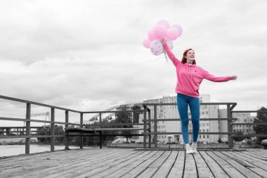 Pembe balonlu rıhtımda dururken gülümseyen mutlu genç kız