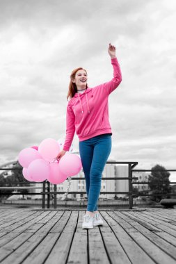 İskelede duran ve pembe balonlar tutan gülümseyen kız