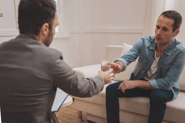 Helpful therapist handing glass of water to his stressed client — Stock Photo, Image