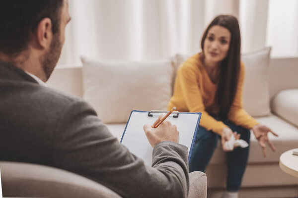 Attentive psychologist. Attentive psychologist holding pencil in his hands making written notes while listening to his client