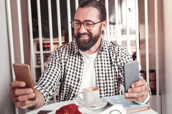 Usmívající se muž pomocí dvou smartphonů při práci — Stock fotografie
