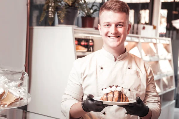 Confeiteiro sorrindo servindo o croissant com um creme — Fotografia de Stock