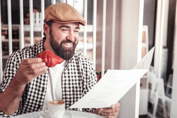 Muž, výběr položek v menu při jídle croissant — Stock fotografie