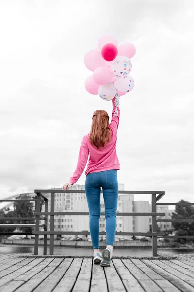 Lungo dai capelli sottile ragazza in piedi sul molo e tenendo mazzo di palloncini — Foto Stock