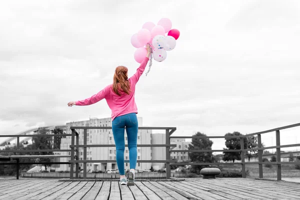 Entspanntes junges Mädchen, das auf der Seebrücke rosa Luftballons in die Höhe hält — Stockfoto