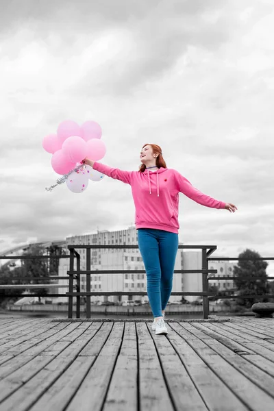 Friedliches Mädchen sieht glücklich aus, während es mit rosa Luftballons spaziert — Stockfoto